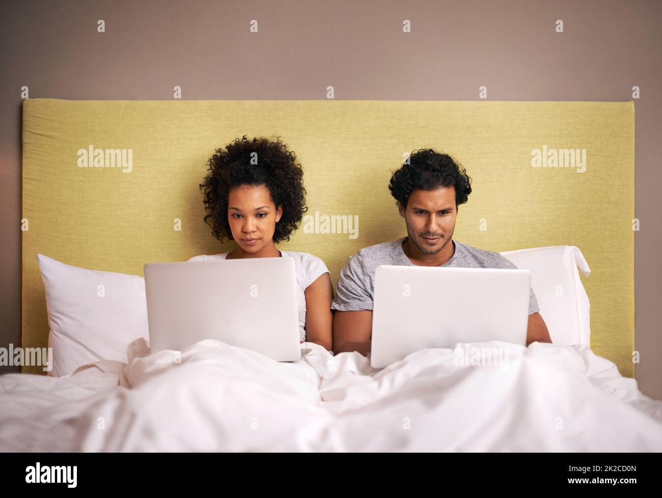 Sitzungssaal im Schlafzimmer. Ein junges Paar im Bett mit ihren Laptops. Stockfoto