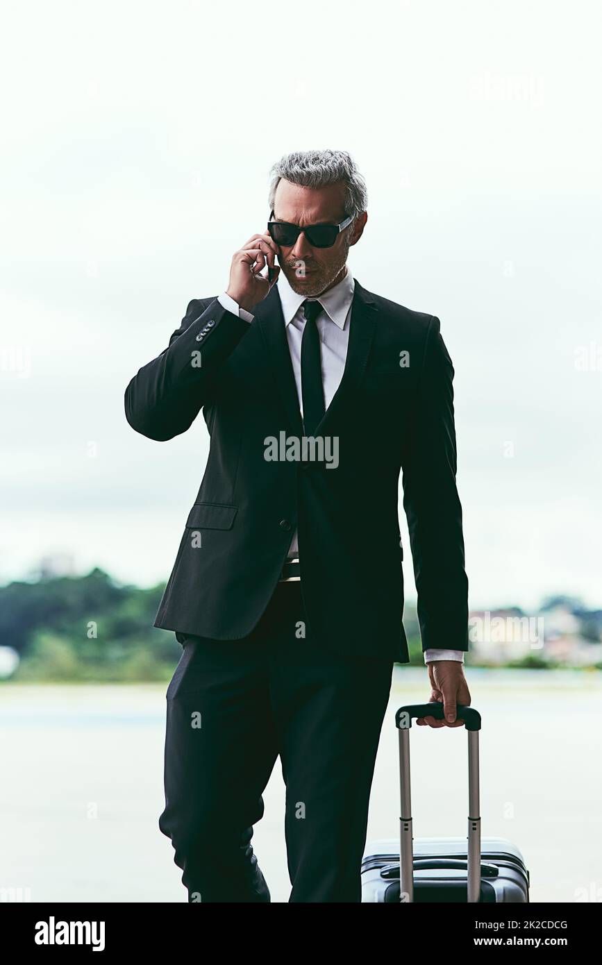 Ich bin gerade gelandet. Eine kurze Aufnahme eines gutaussehenden, reifen Geschäftsmanns, der mit seinem Gepäck außerhalb des Flughafens läuft. Stockfoto