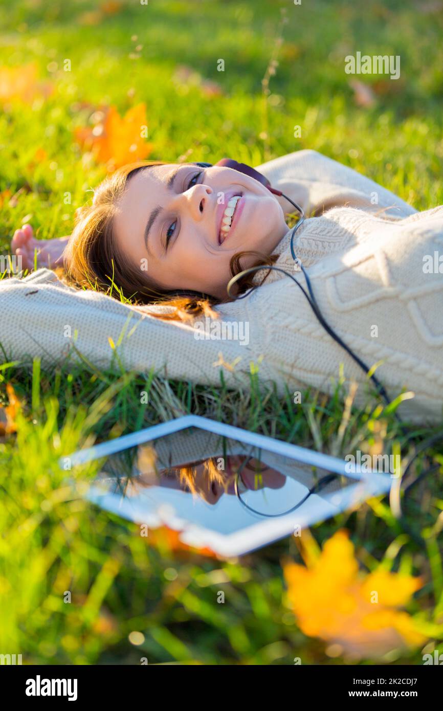 Sie liebt ihre Melodien. Eine attraktive junge Frau, die im Freien Musik auf ihrem digitalen Tablet hört. Stockfoto