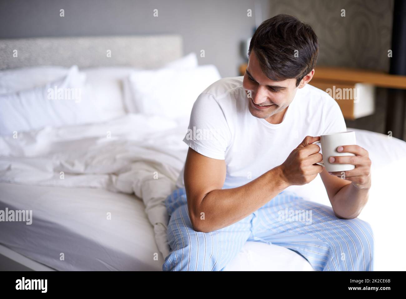 Kaffee ist der beste Weckruf. Eine kleine Aufnahme eines hübschen jungen Mannes, der Kaffee am Rand seines Bettes trinkt. Stockfoto