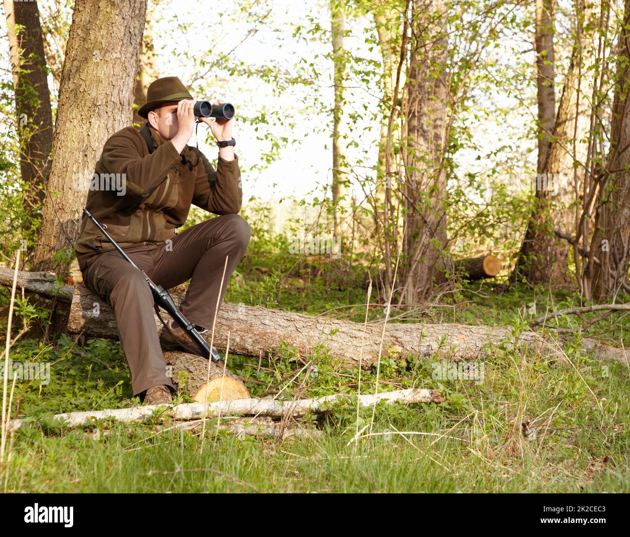 Wildtierjagd erfordert Geduld. Ein Wildhüter, der durch sein Fernglas schaut, während er auf einem Baumstamm sitzt. Stockfoto