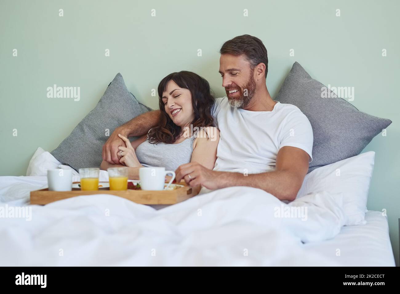 Wo sollen wir anfangen? Aufnahme eines fröhlichen jungen Paares, das morgens im Bett sitzt und das Frühstück zusammen genießt. Stockfoto