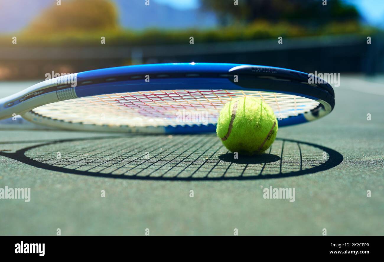 Es ist der perfekte Tag für ein Tennisspiel. Kurzer Schuss eines Tennisschlägers und eines Balls auf einem leeren Platz während des Tages. Stockfoto