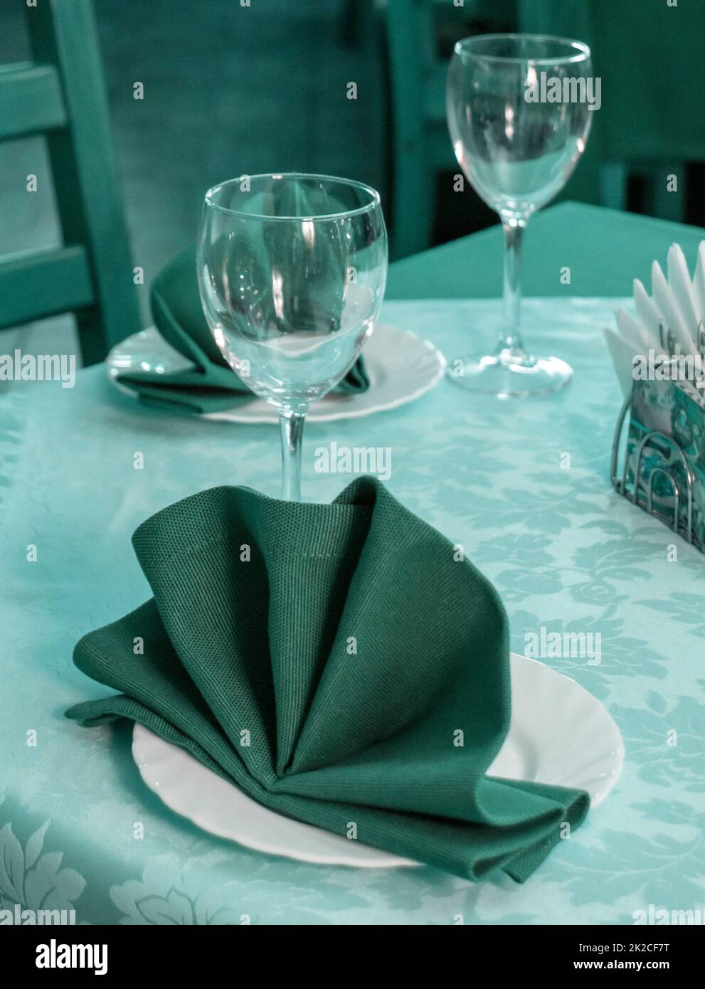 Nahaufnahme eines romantischen Servierens in einem Restaurant, Tisch mit Servietten und Gerichten, abends grün-blau getönt, vertikal Stockfoto