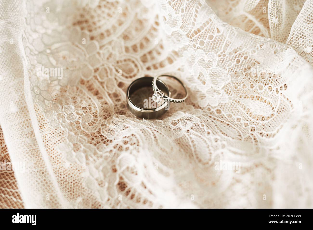 Sie symbolisieren unser lebenslanges Engagement füreinander. Stillleben von zwei schönen Eheringen auf einem Hochzeitskleid. Stockfoto