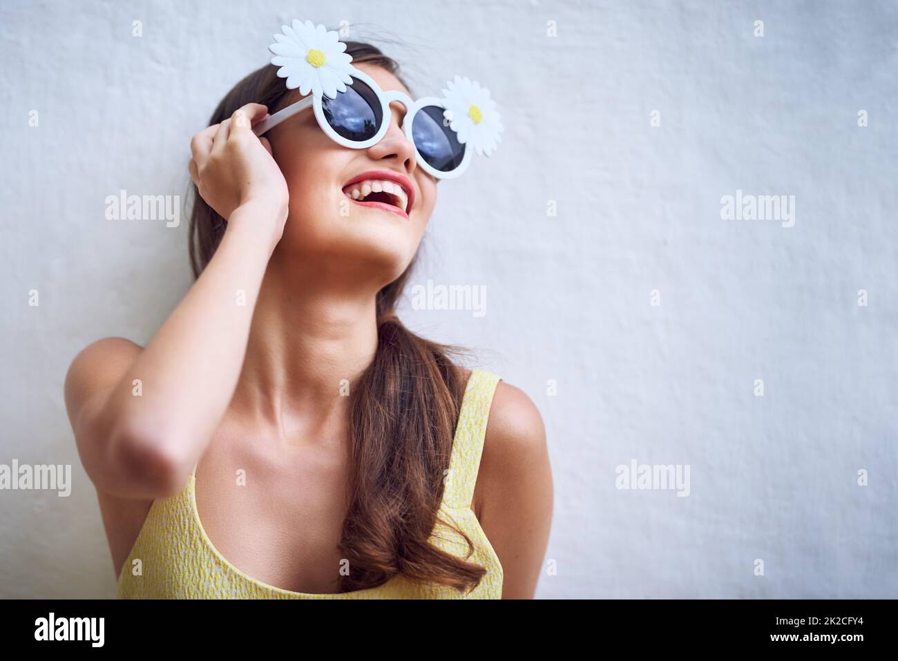Wohin sie auch geht, die Sonne geht. Studioaufnahme einer fröhlichen jungen Frau, die eine Sonnenbrille trägt und vor einem grauen Hintergrund posiert. Stockfoto