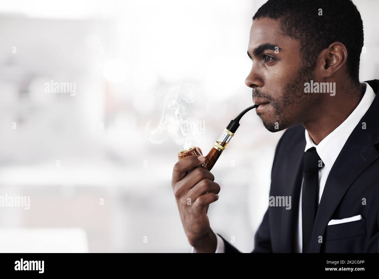 Stilvolles Dampfen. Ein junger Geschäftsmann, der in einem Büro eine elektronische Pfeife raucht. Stockfoto