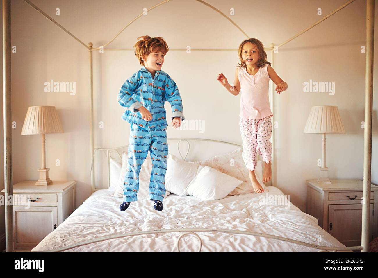 Ich kann höher springen als Ihr. Aufnahme von zwei kleinen Kindern, die zu Hause auf einem Bett zusammenspringen. Stockfoto