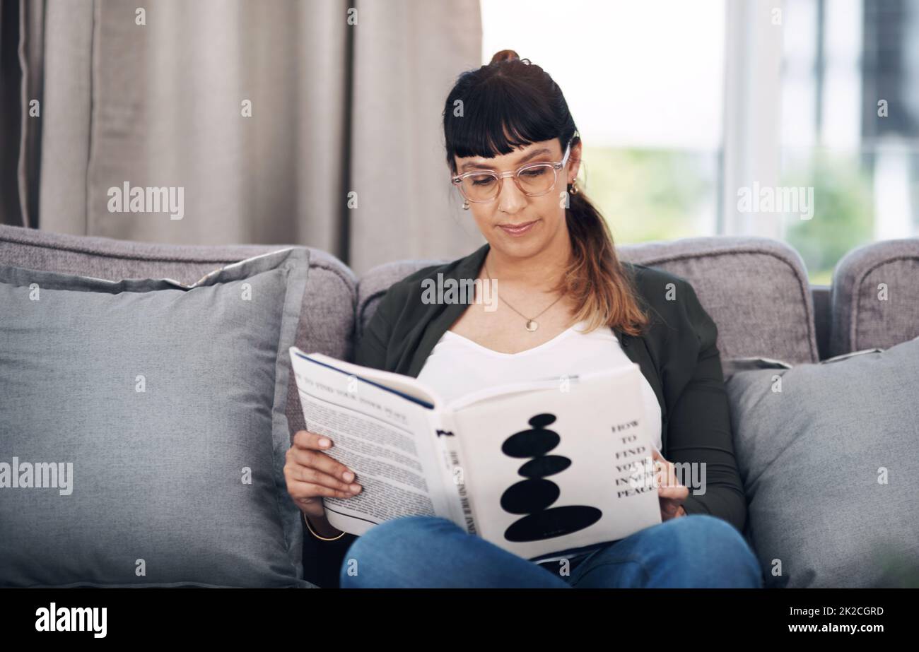 Einmal ein Bücherwurm, immer ein Bücherwurm. Ausgeschnittene Aufnahme einer attraktiven jungen Frau, die allein in ihrem Wohnzimmer sitzt und ein Buch liest. Stockfoto