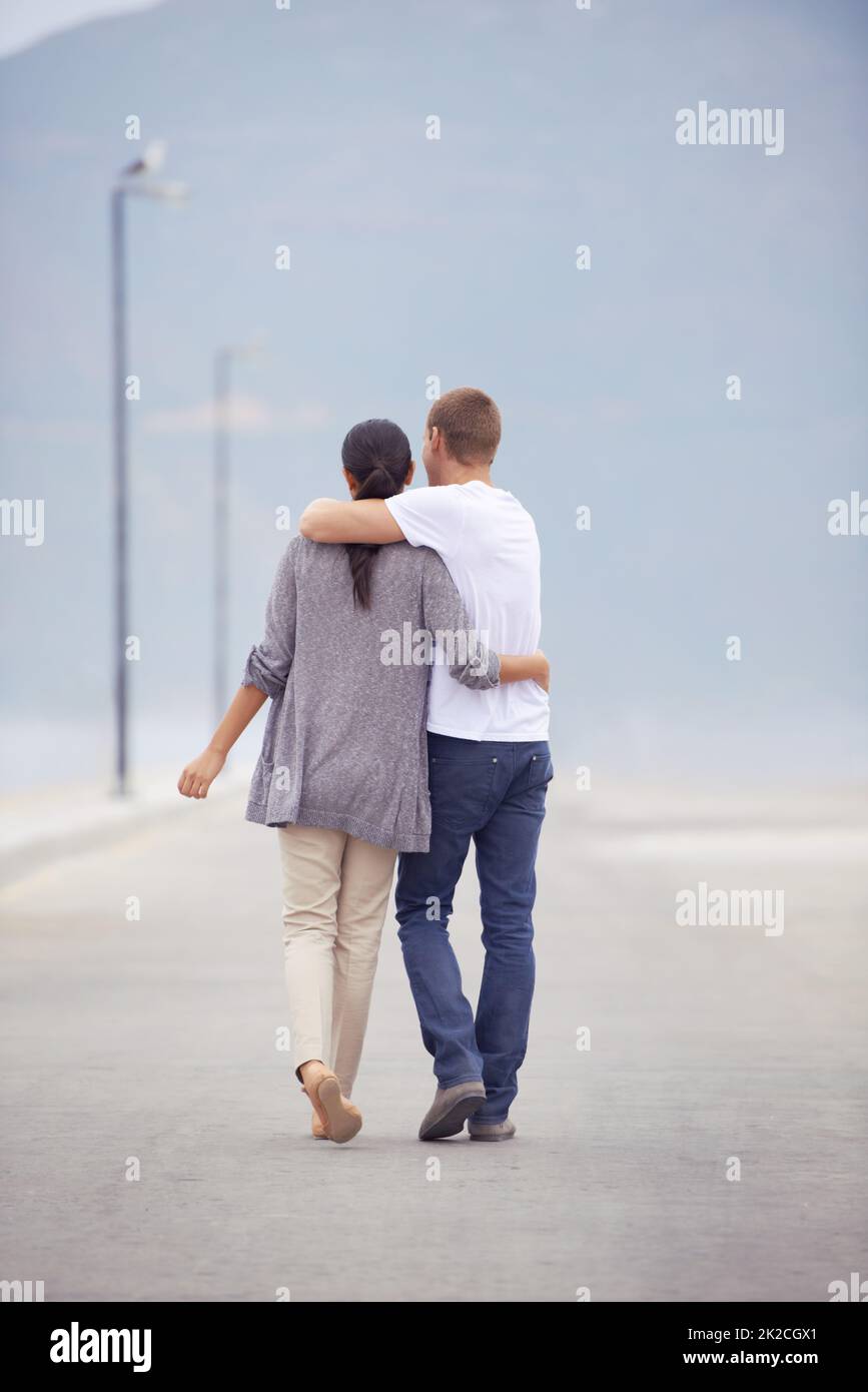 Die junge Liebe ist voller Zuneigung. Lange Rückansicht eines jungen Paares, das an einer Promenade entlang läuft. Stockfoto