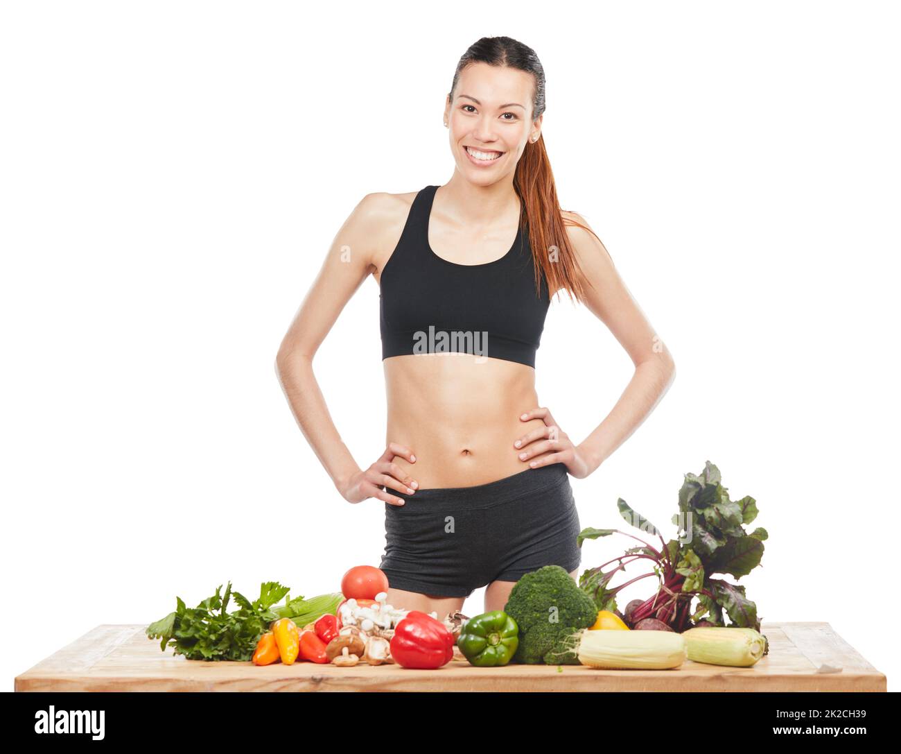 Machen Sie eine gesunde Ernährung Ihre Gewohnheit. Studioporträt einer attraktiven jungen Frau, die mit einem Tisch voller Gemüse vor weißem Hintergrund posiert. Stockfoto