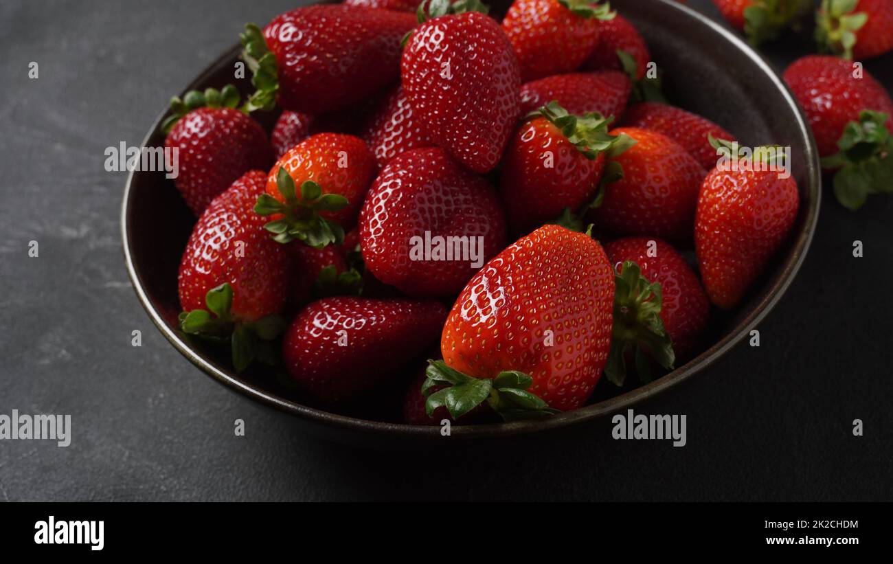 Erdbeere frische Bio-Früchte auf einem Teller. Erdbeeren mit Blättern. Isoliert auf schwarzem Hintergrund. Stockfoto