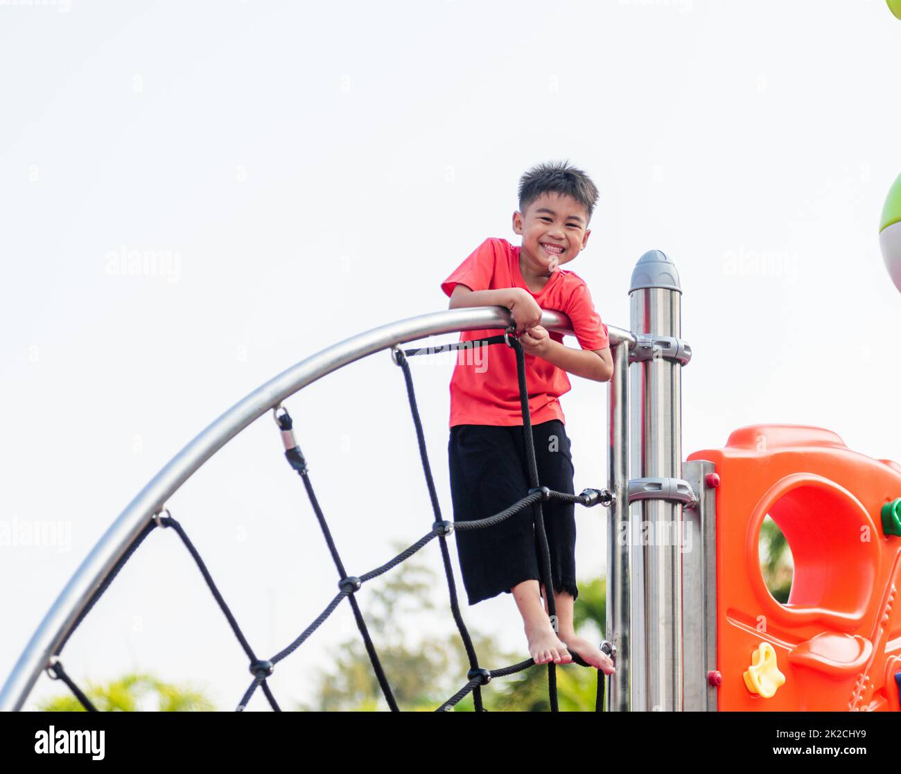 Asiatisches Kind lächelt beim Klettern draußen auf dem Spielplatz Stockfoto