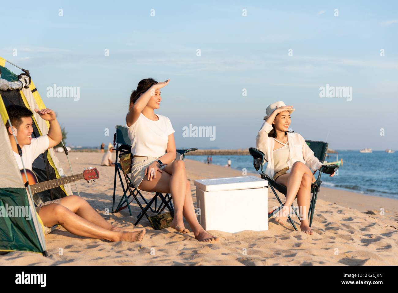 Glückliche Freunde mit Drinks im Camp und gemeinsam lachen im Urlaub am Sandstrand in der Nähe des Campingzelts Urlaubszeit bei Sonnenuntergang Stockfoto