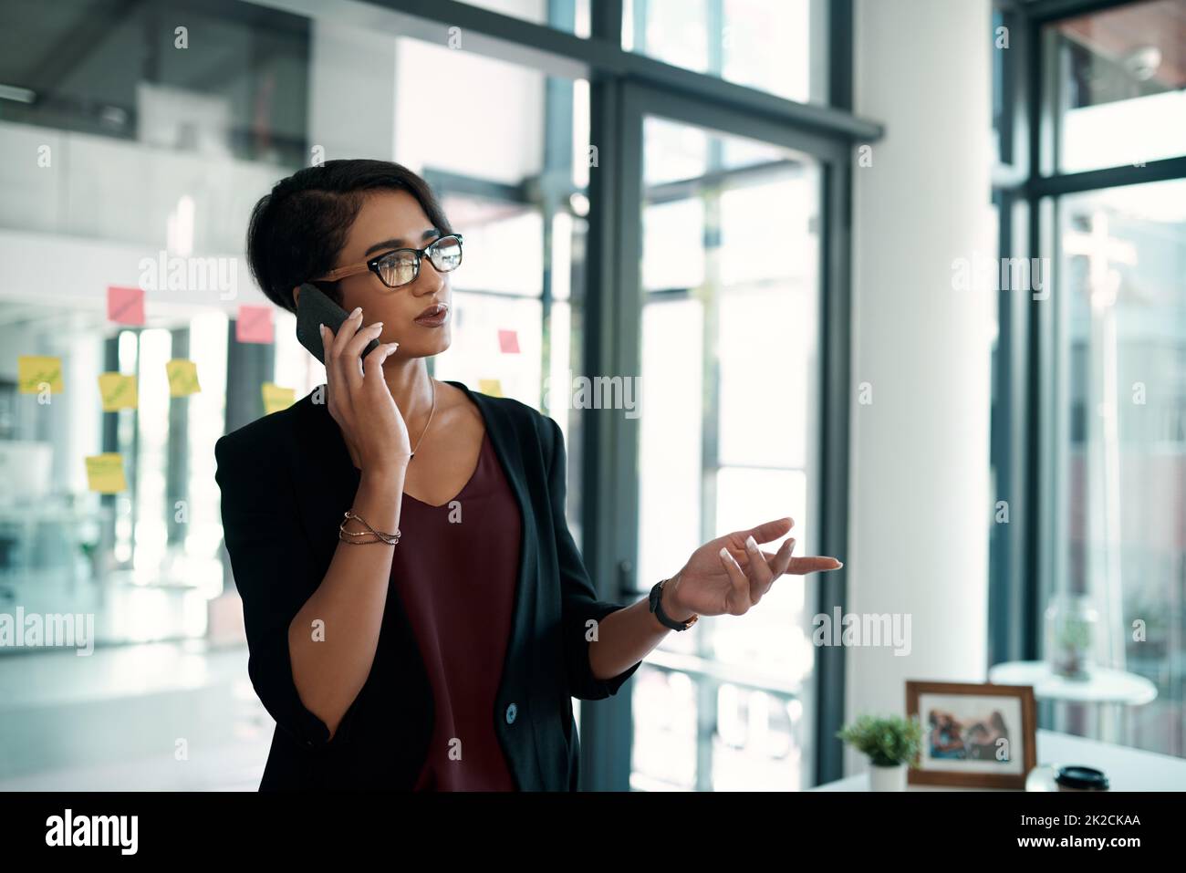 Soll ich die Meetings tauschen? Freigestellte Aufnahme einer attraktiven jungen Geschäftsfrau, die allein in ihrem Büro steht und mit ihrem Handy spricht. Stockfoto