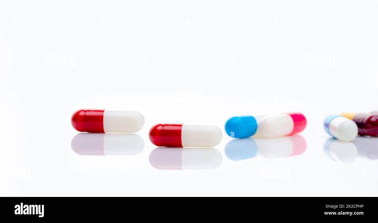 Rot-weiße Antibiotikakapsel auf verschwommenem, mehrfarbigen Kapselhintergrund. Antibiotikaresistenzkonzept. Horizontales Banner Pharmazie. Verschreibungspflichtige Medikamente. Pharmazeutische Industrie. Gesundheitswesen. Stockfoto