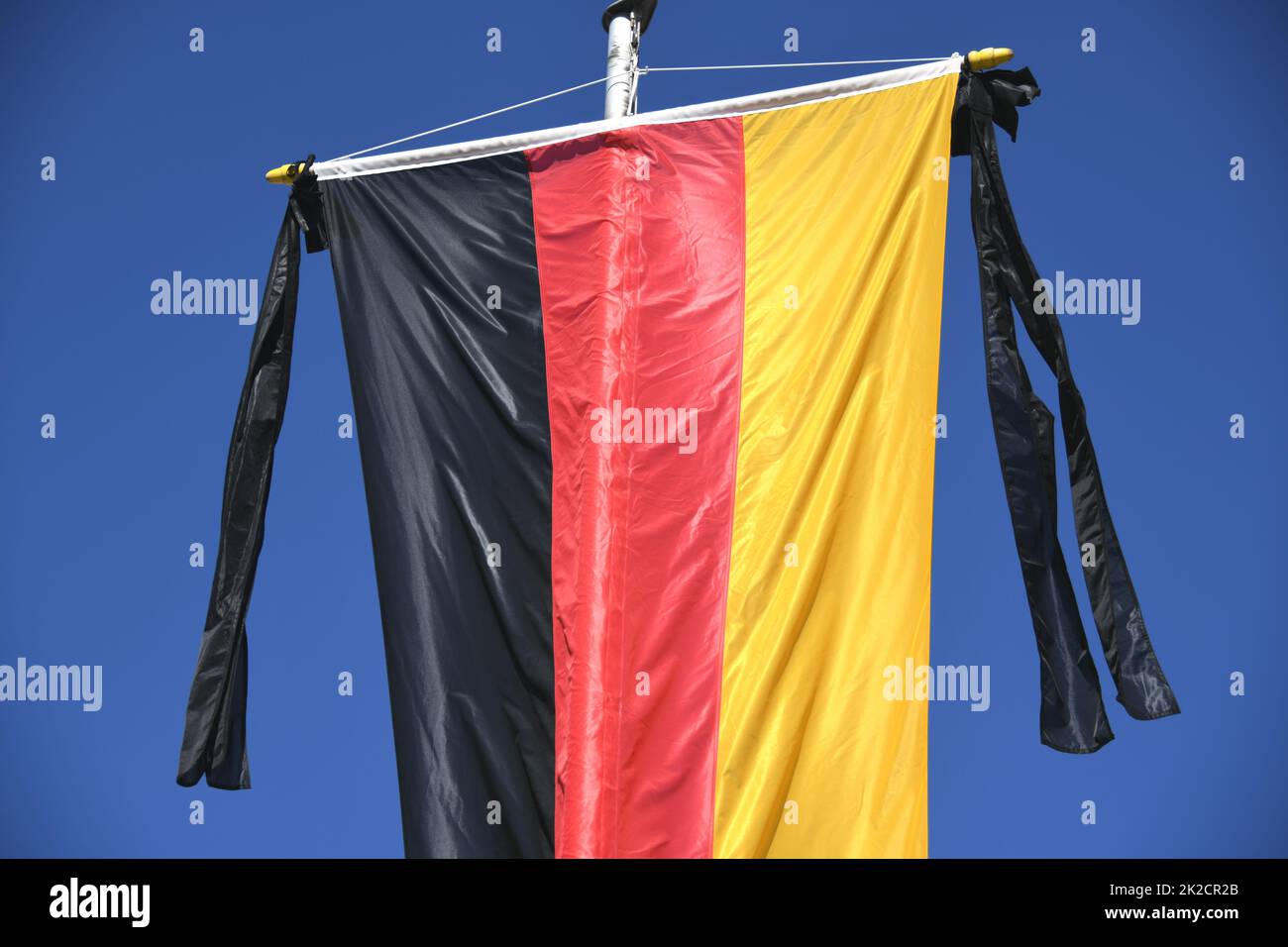 Die Nationalflagge der Bundesrepublik Deutschland, schwarz, rot, goldfarben, hängt an der Fahnenstange. Als Symbol der nationalen Trauer ist das Trauerband mit zwei schwarzen Bändern an der Flagge befestigt. Stockfoto