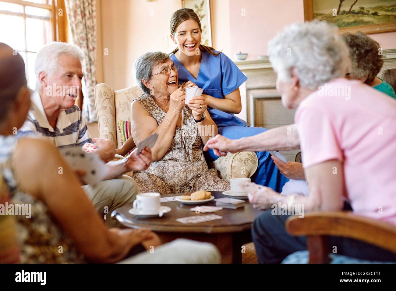 Die Spannung hält das Spiel spannend. Aufnahme einer Gruppe glücklicher Senioren, die in ihrem Altersheim ein Kartenspiel spielen, während eine Krankenschwester zuschaut. Stockfoto