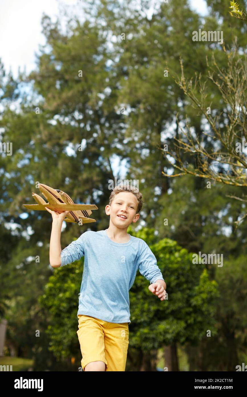 In die Luft. Aufnahme eines Jungen, der mit einem Spielzeug-Flugzeug durch einen Park läuft. Stockfoto