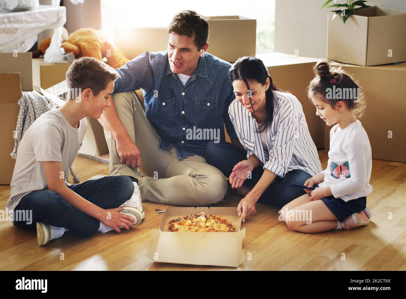 Essen eins und viele weitere werden kommen. Aufnahme einer glücklichen jungen Familie, die gemeinsam Pizza in ihrem neuen Zuhause hat. Stockfoto