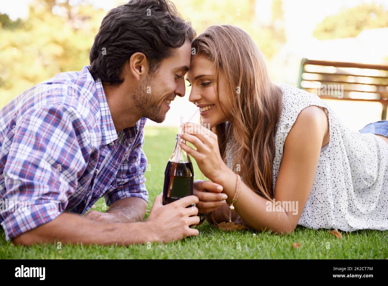 Junge Liebe. Ein glückliches junges Paar, das im Park zusammen Cola nippt. Stockfoto