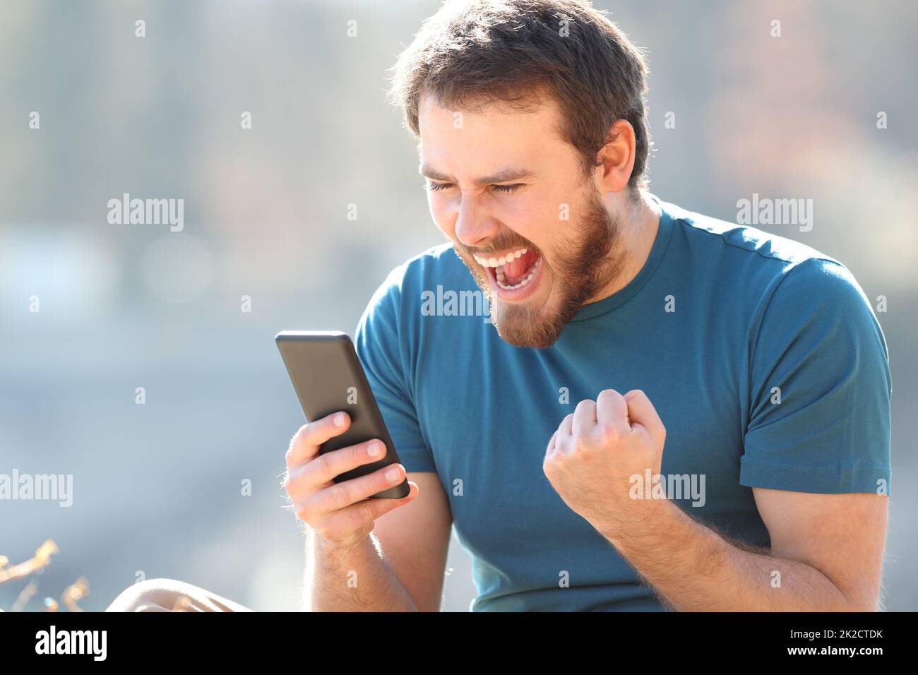 Aufgeregter Mann, der im Freien gute Nachrichten am Telefon findet Stockfoto