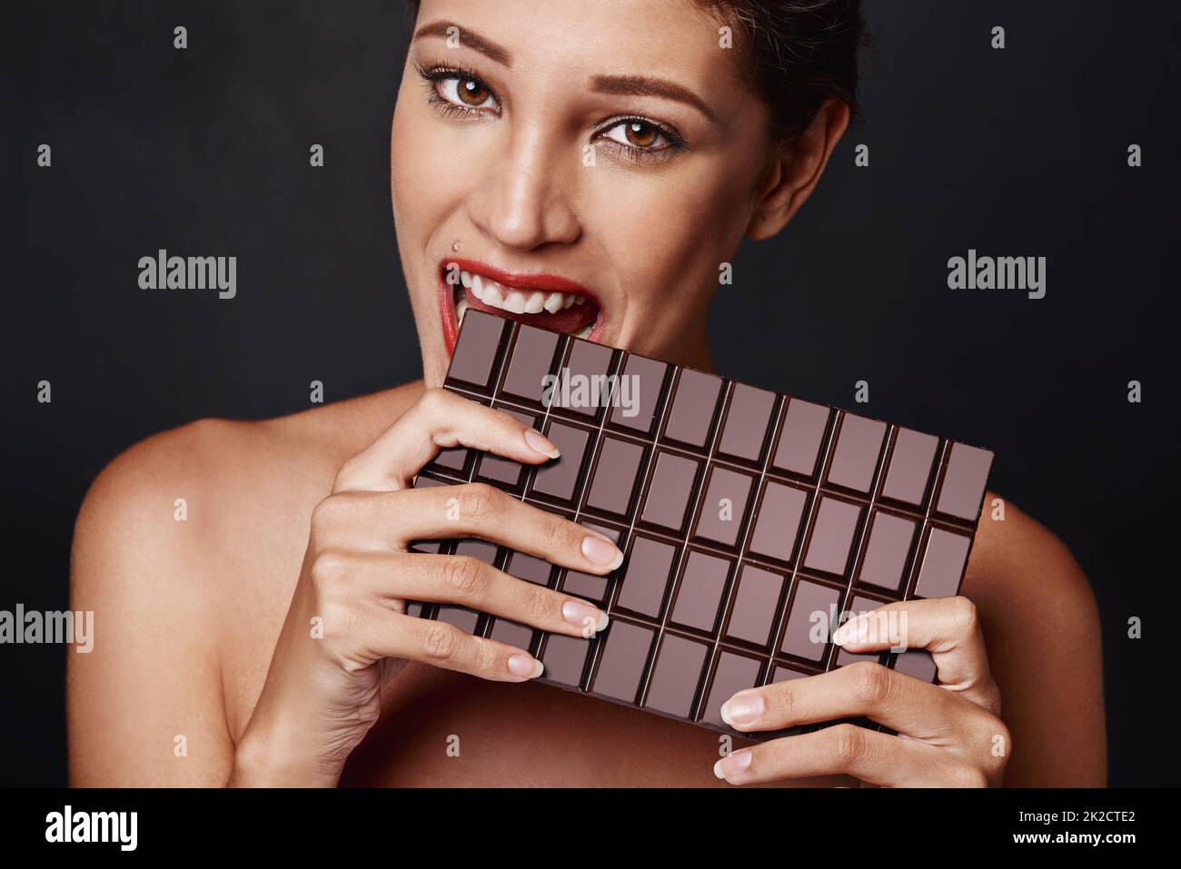 Ja, Größe zählt. Studioaufnahme einer attraktiven jungen Frau, die in eine Schokoladenplatte beißt. Stockfoto