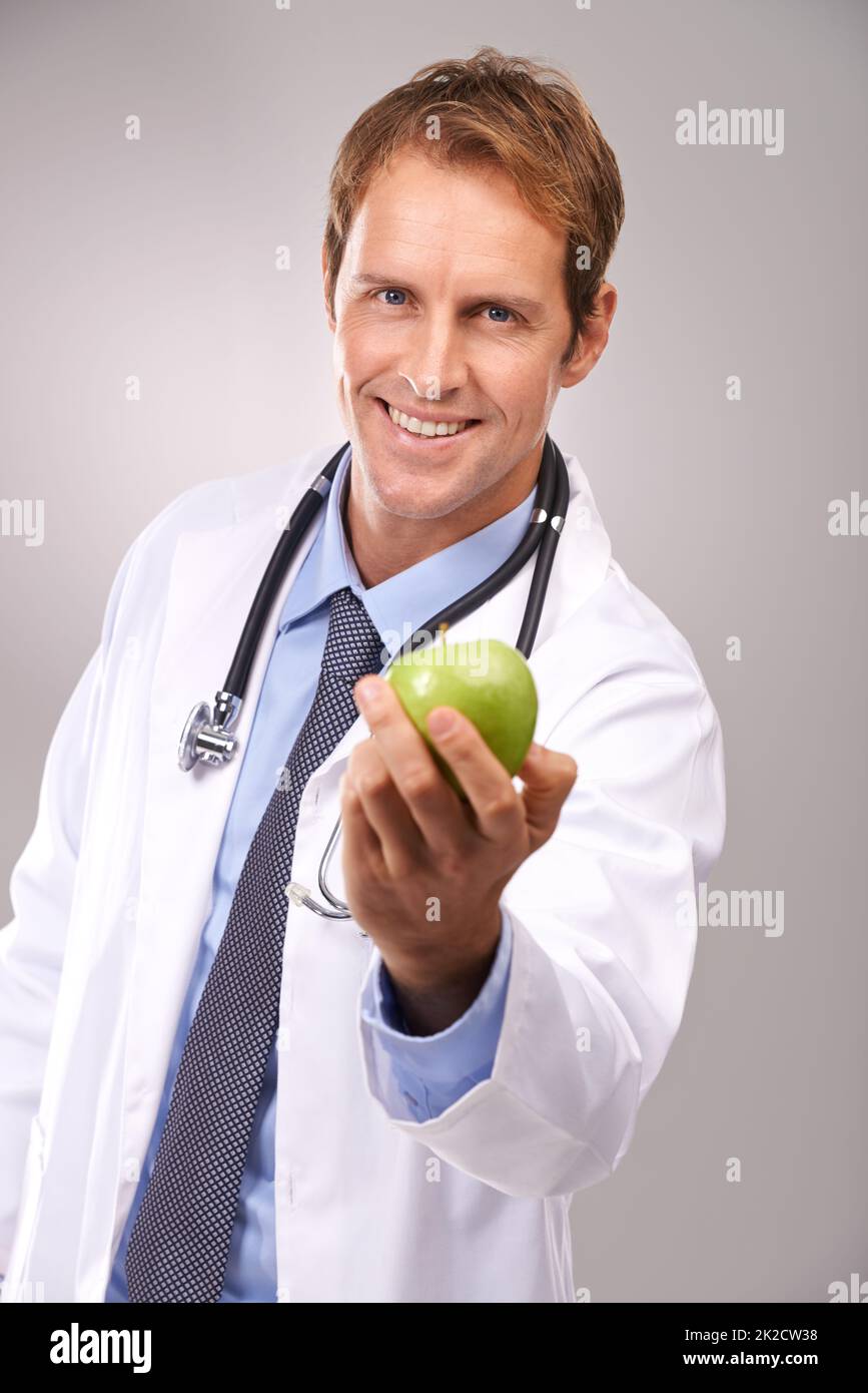 Eines am Tag wird mich davon fernhalten. Studioporträt eines hübschen jungen Arztes, der einen grünen Apfel aushält. Stockfoto