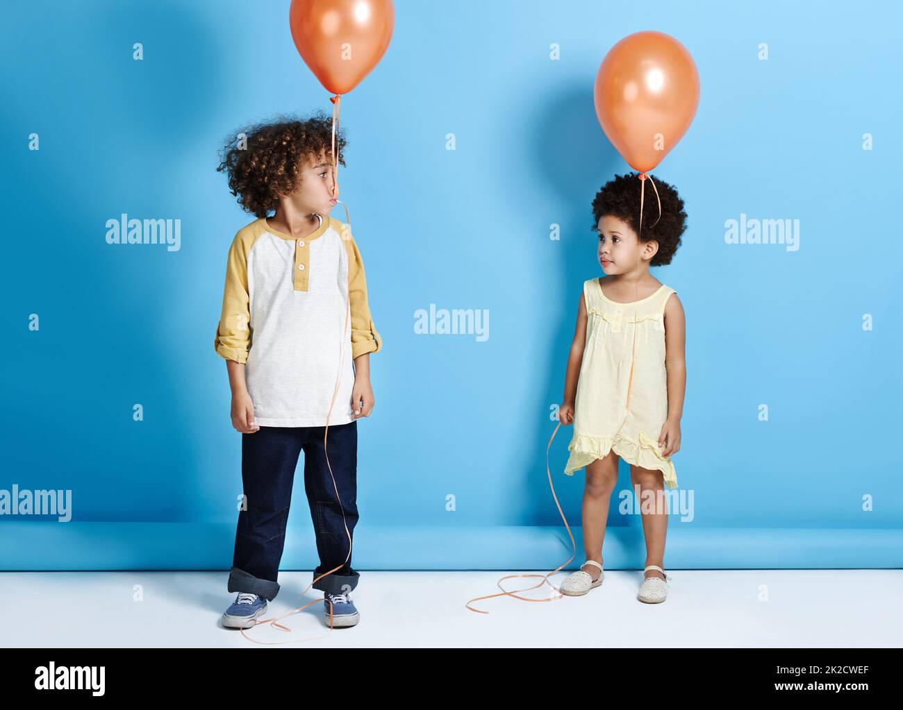 Schau, keine Hände. Aufnahme eines kleinen Mädchens und Jungen, die einen Ballon auf einem blauen Hintergrund halten. Stockfoto