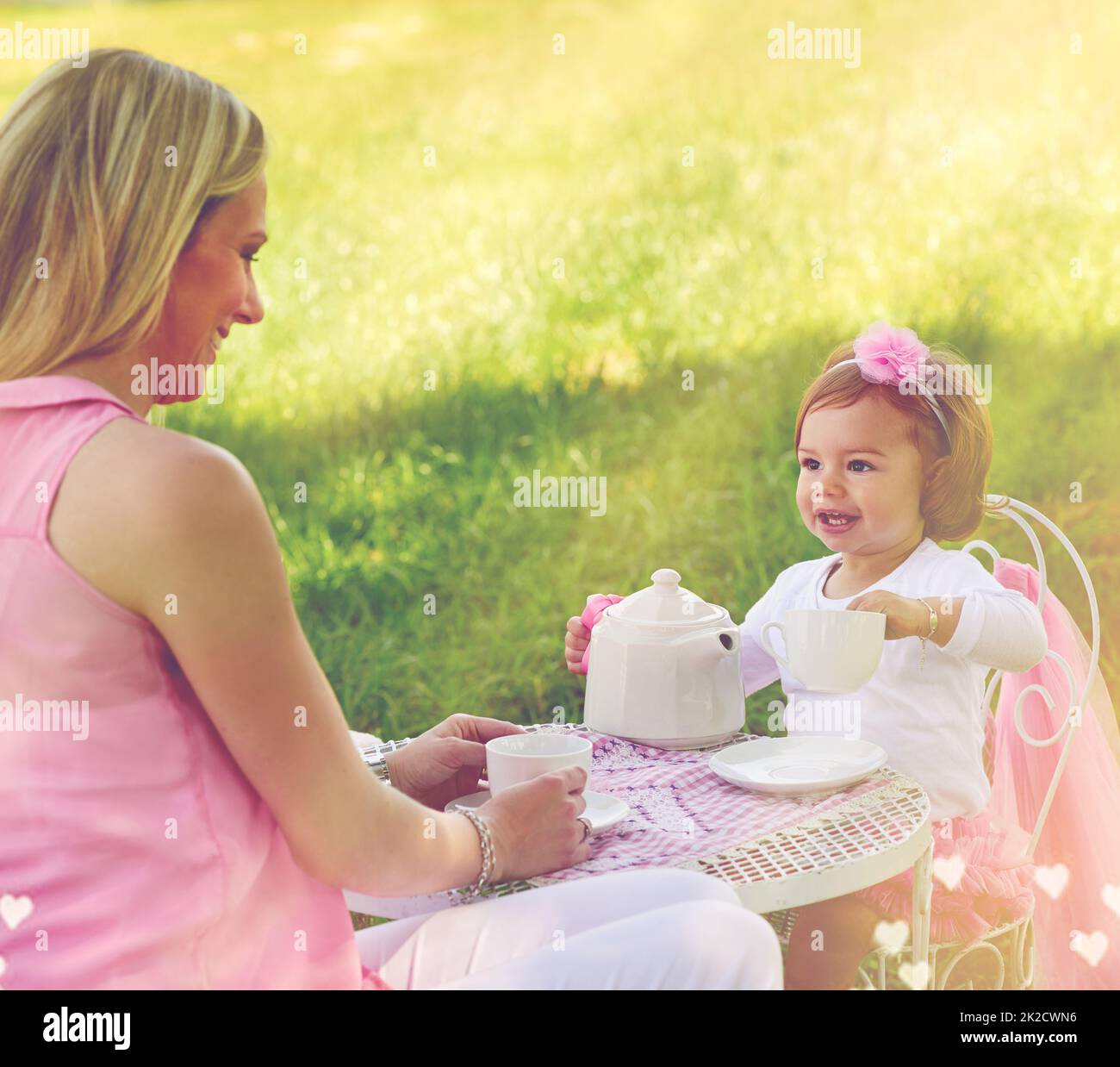 Lasst mich Euch eine Tasse Tee gießen. Aufnahme einer Mutter und ihres niedlichen kleinen Mädchens, die draußen auf dem Rasen eine Teeparty feiern. Stockfoto