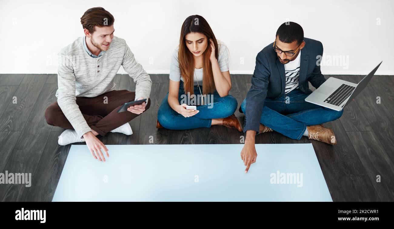 Alles begann mit einem Brainstorming. Studioaufnahme einer Gruppe junger Menschen, die auf dem Boden sitzen und auf leerem Papier arbeiten. Stockfoto