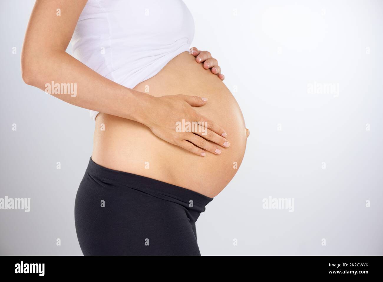 Jetzt jeden Tag Verkürztes Profil einer Schwangeren, die ihren Bauch liebevoll hält. Stockfoto