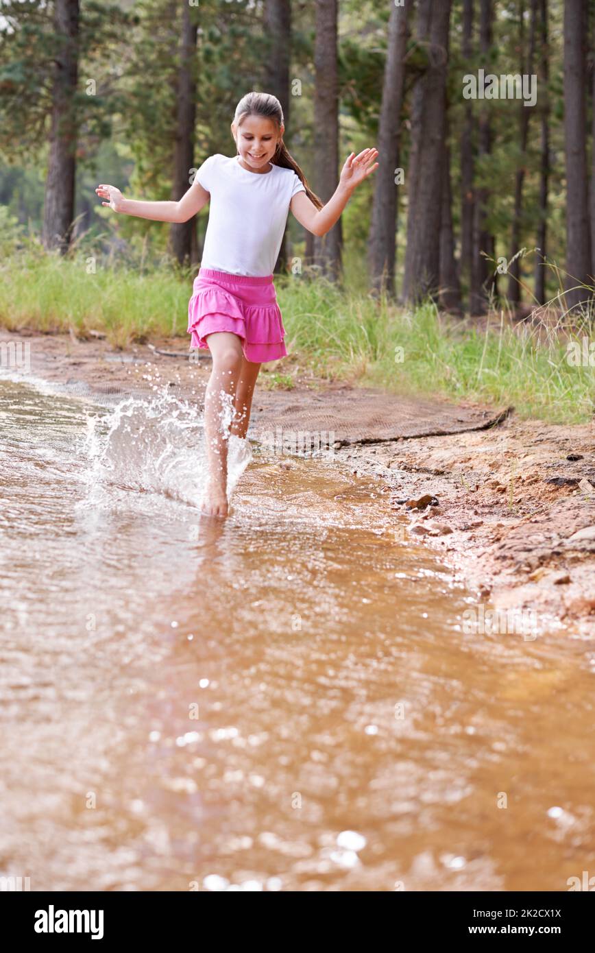 Herumplanschen macht so viel Spaß. Ein niedliches kleines Mädchen, das durch einen Wildnisstrom läuft. Stockfoto