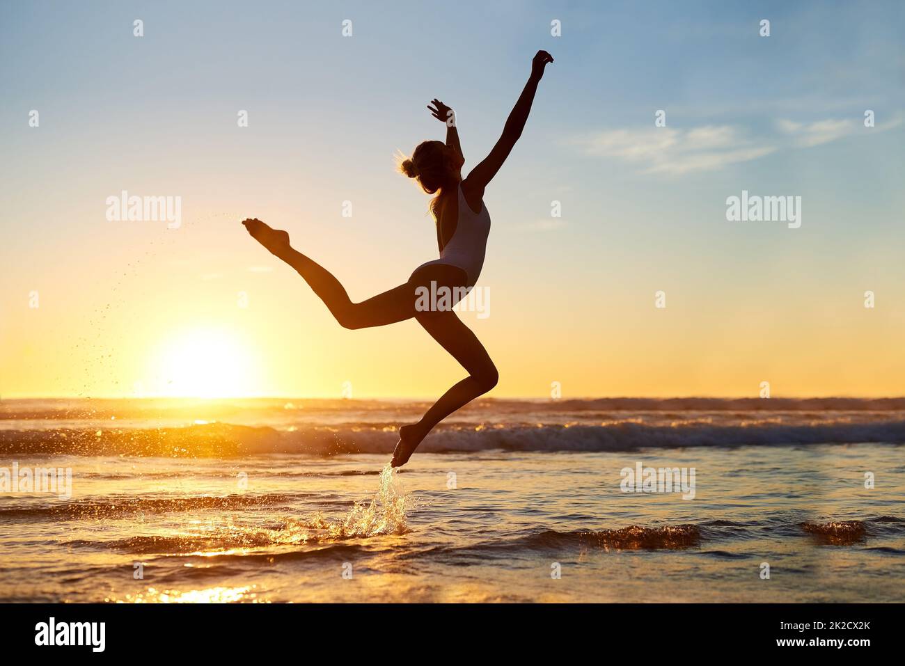 Du bist frei, wer auch immer du bist. Aufnahme einer jungen Frau, die gegen einen wunderschönen Sonnenuntergang am Strand in die Luft springt. Stockfoto