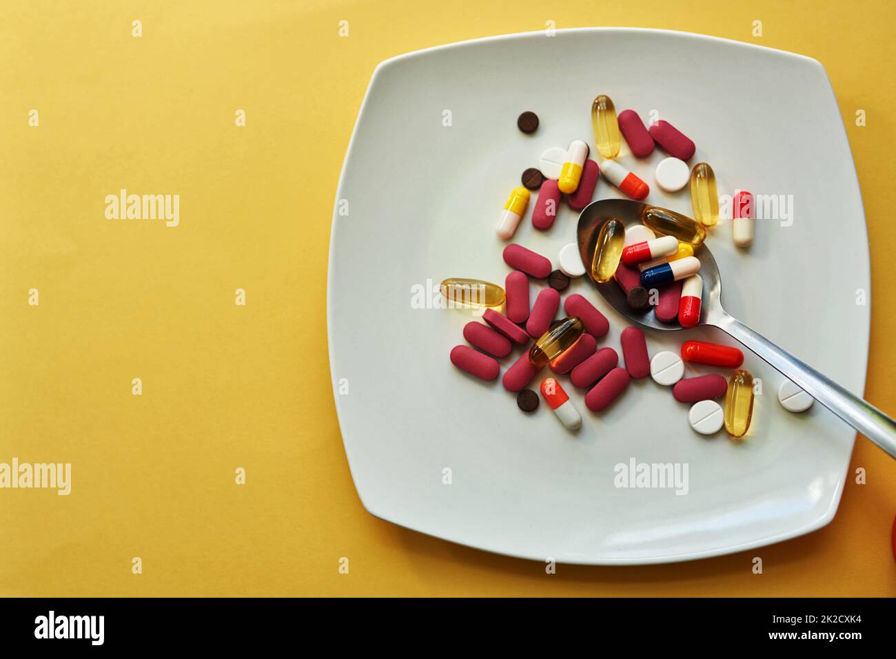 Wenn Gewichtsverlust wird zu Ernährungsverlust. Studioaufnahme von Medikamenten, die auf einem Teller mit einem Löffel vor gelbem Hintergrund serviert werden. Stockfoto