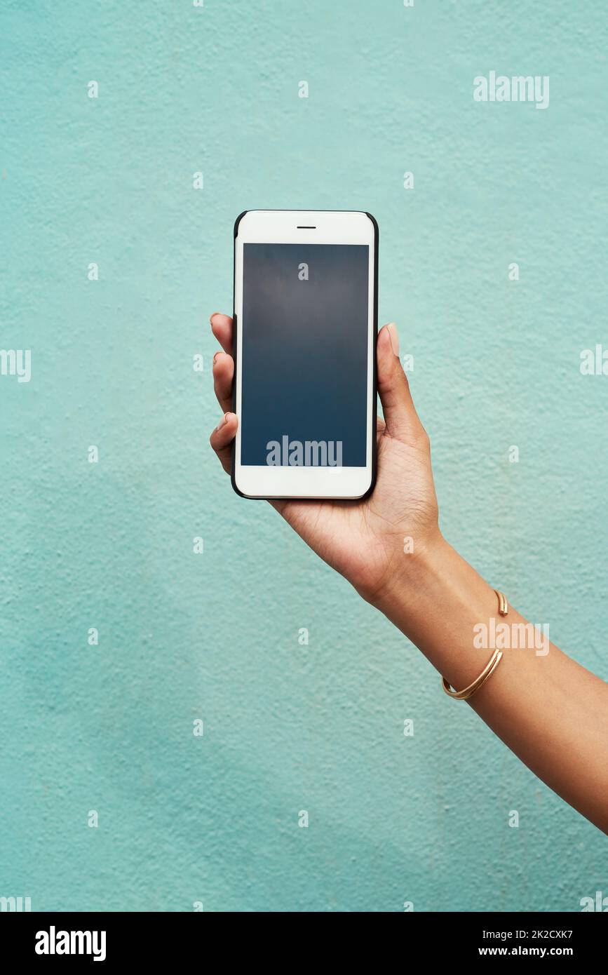 Technologie macht die Welt zugänglicher. Ausgeschnittene Aufnahme einer nicht erkennbaren Frau, die ihr Mobiltelefon vor einem blauen Hintergrund in der Stadt hält. Stockfoto