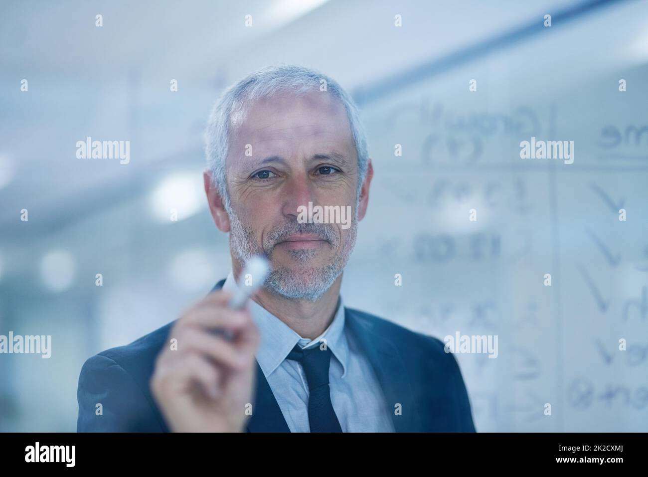 Seine Erfolgsrechnungen kommen alle zusammen. Ausgeschnittene Aufnahme eines reifen Geschäftsmannes, der Figuren auf einem Glasschirm schreibt. Stockfoto