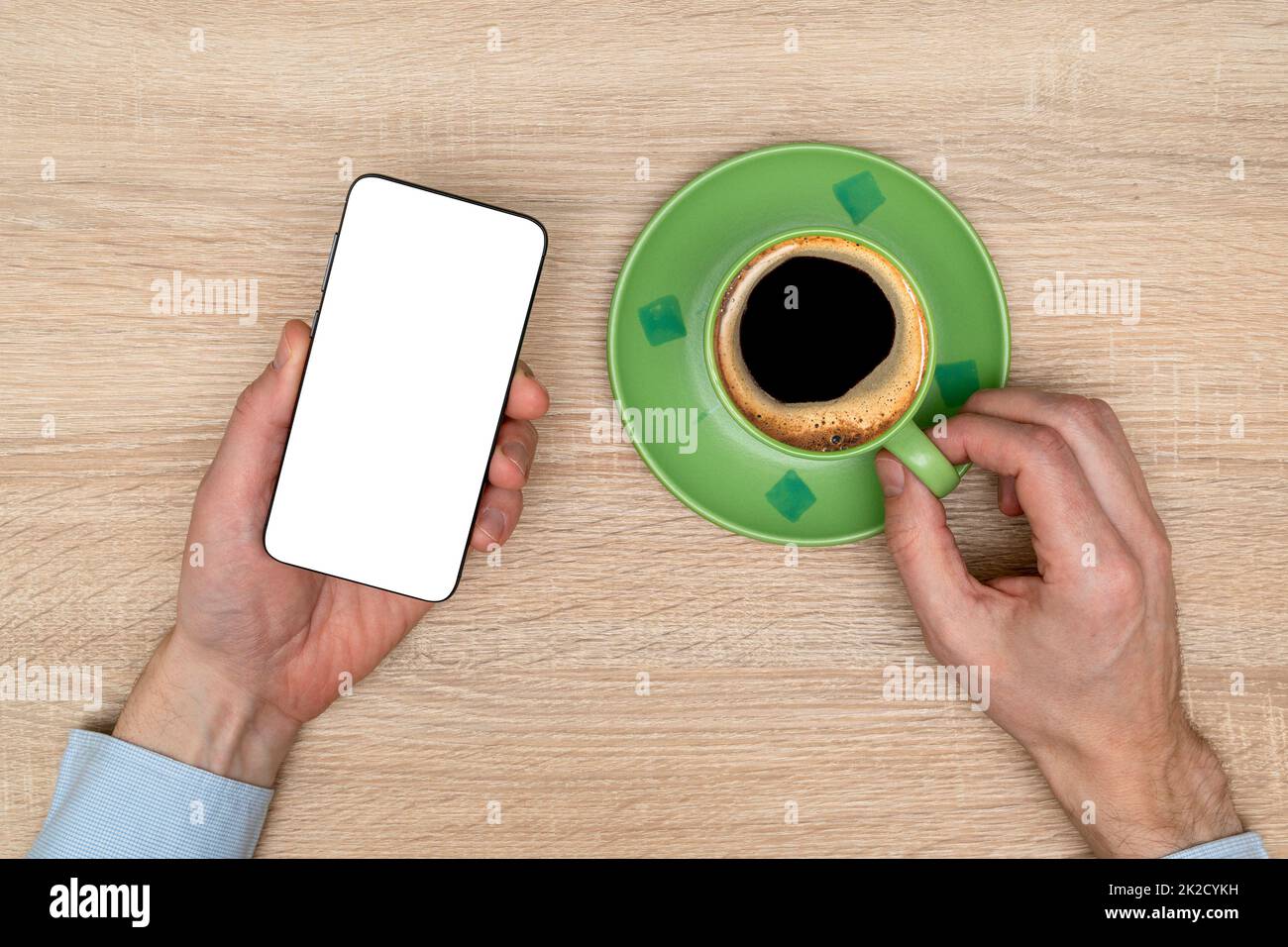 Hand eines Geschäftsmannes, der beim Trinken von schwarzem Kaffee ein Mobiltelefon mit weißem Bildschirm hält Stockfoto