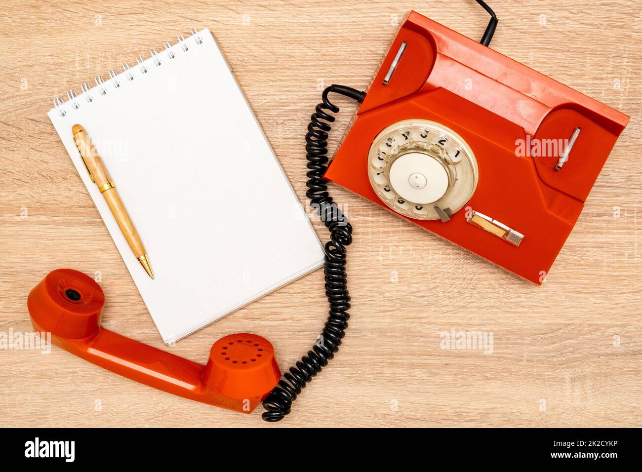 Orangefarbenes Drehtelefon und leeres Notizbuch auf Holzhintergrund Stockfoto