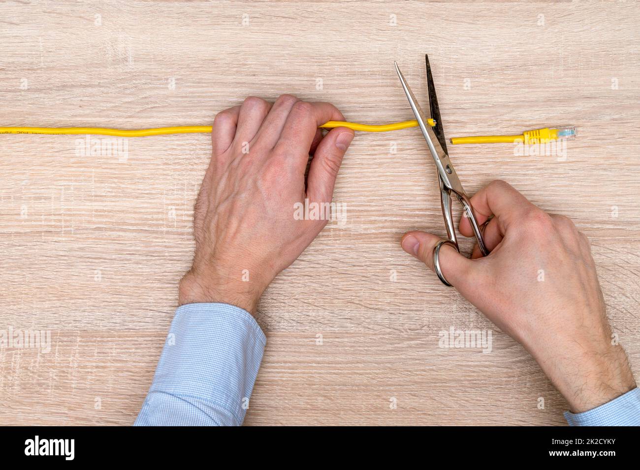 Internetzensor schneidet ein gelbes Netzwerkkabel über Holzhintergrund Stockfoto