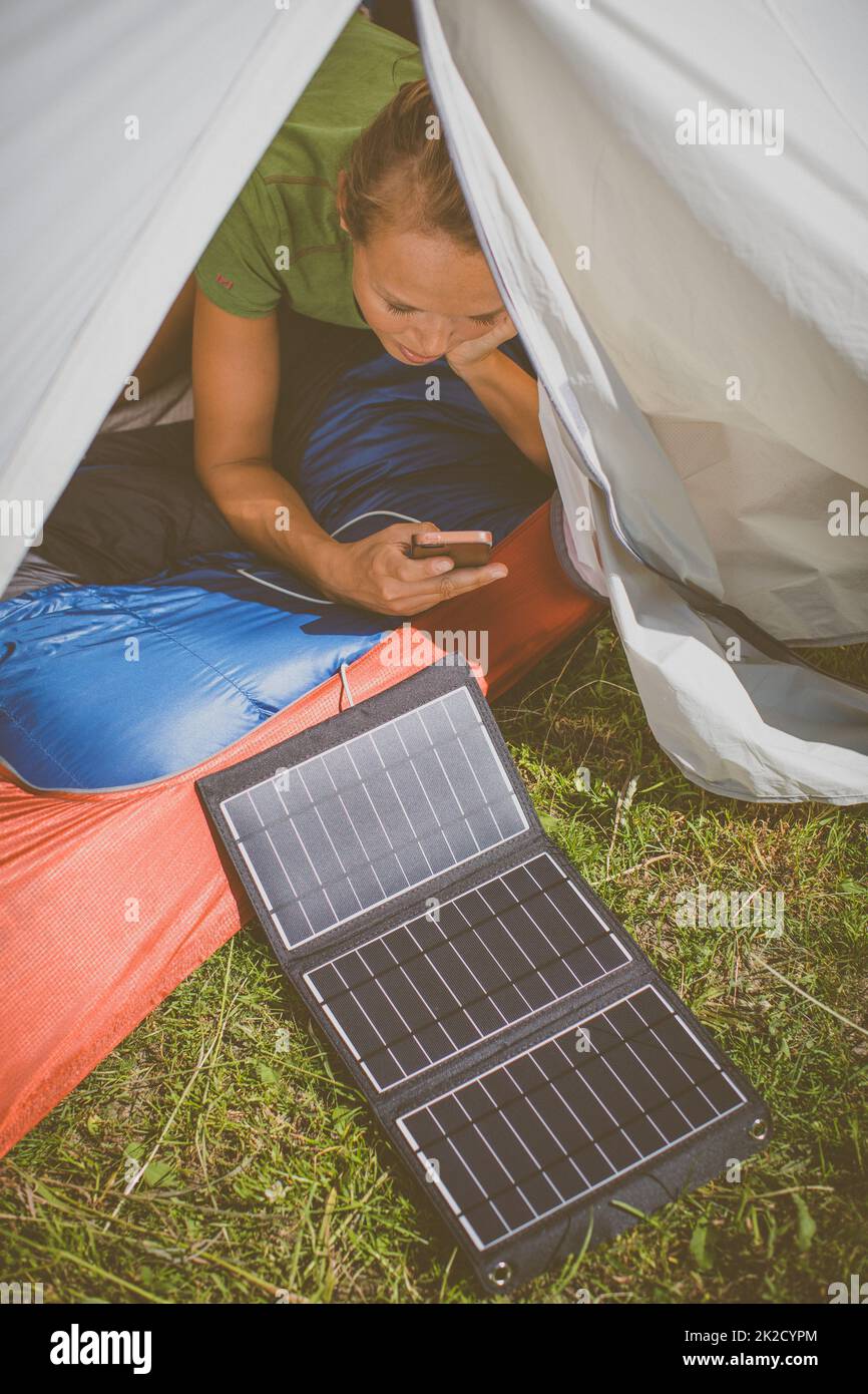 Handy wird während einer Fahrt im Freien mit einem Solarladegerät in einem Zelt aufgeladen Stockfoto