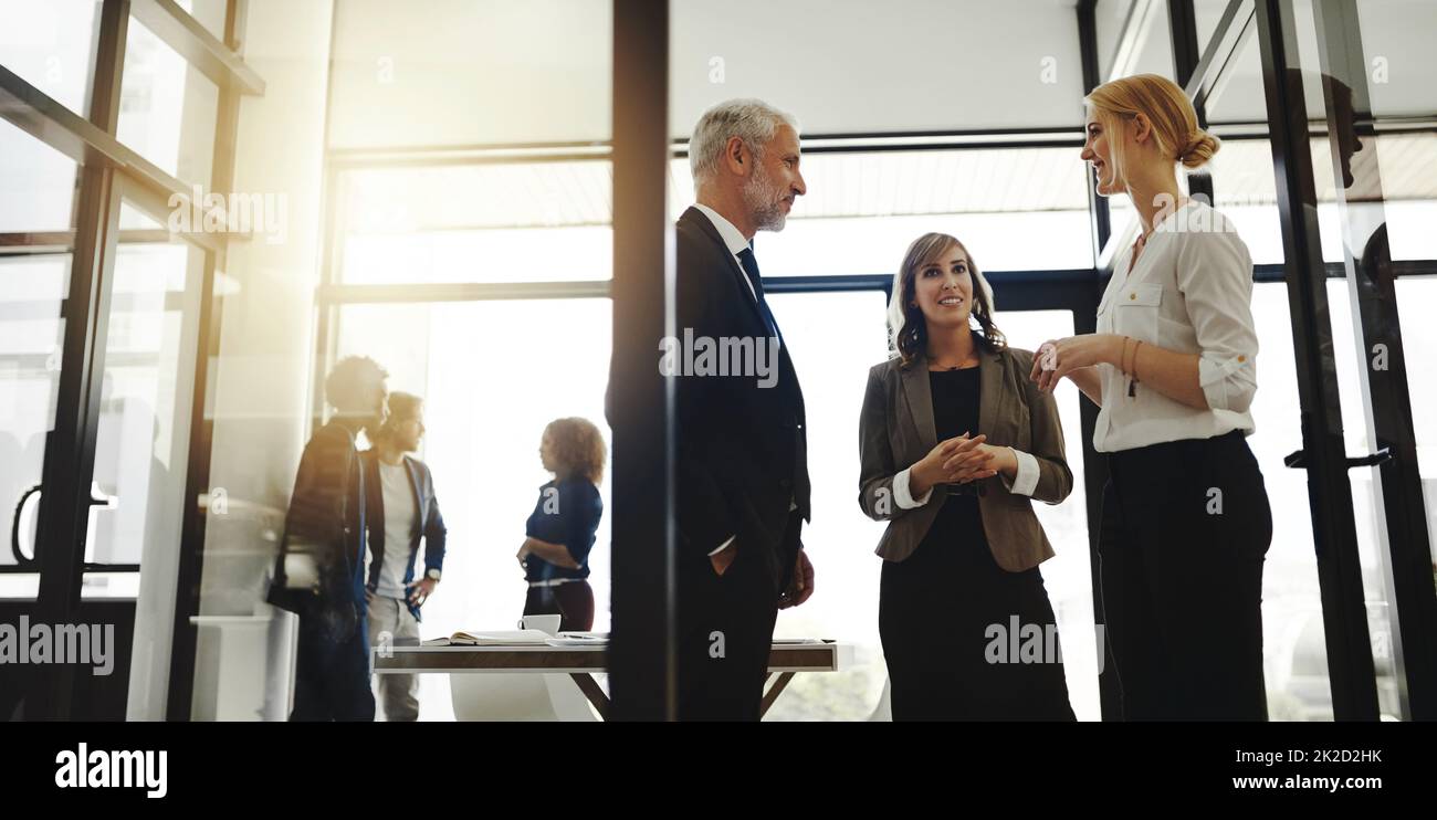 Unternehmensgespräche. Eine kurze Aufnahme von drei Geschäftsleuten, die im Büro stehen und sprechen. Stockfoto