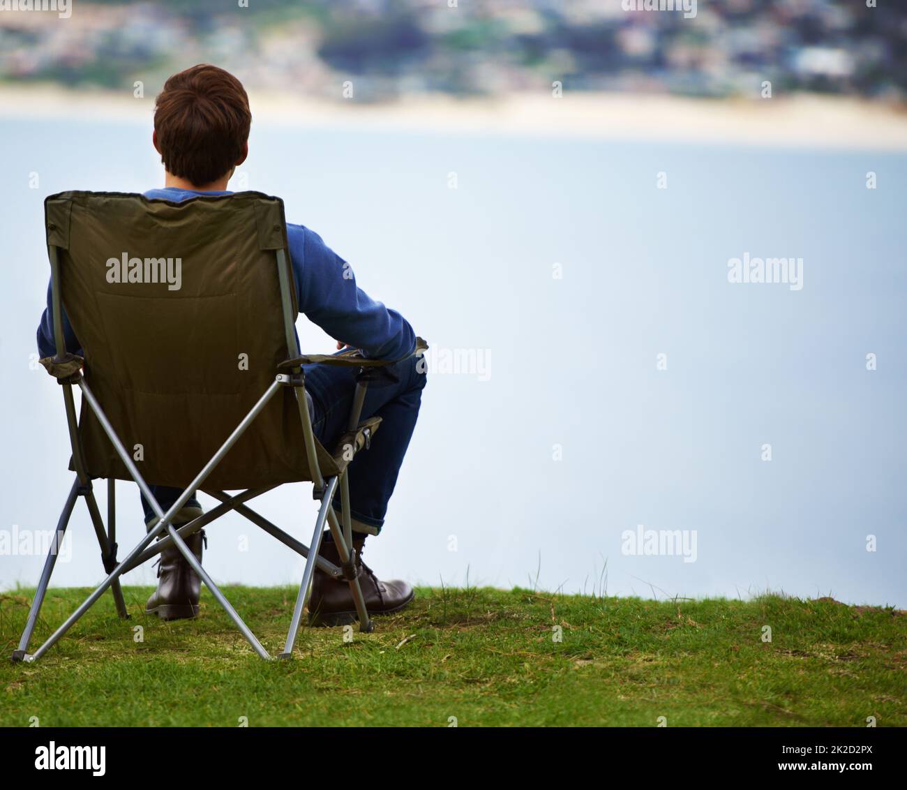 Der perfekte Ort, um die Landschaft zu genießen. Rückansicht eines jungen Mannes, der auf einem Campingstuhl sitzt und die Aussicht betrachtet. Stockfoto