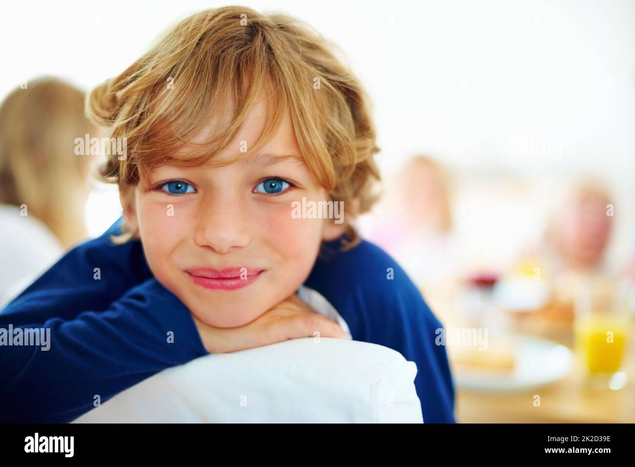 Glücklicher kleiner Junge und seine Familie beim Frühstück im Hintergrund. Nahaufnahme eines glücklichen Jungen und seiner Familie beim Frühstück im Hintergrund. Stockfoto