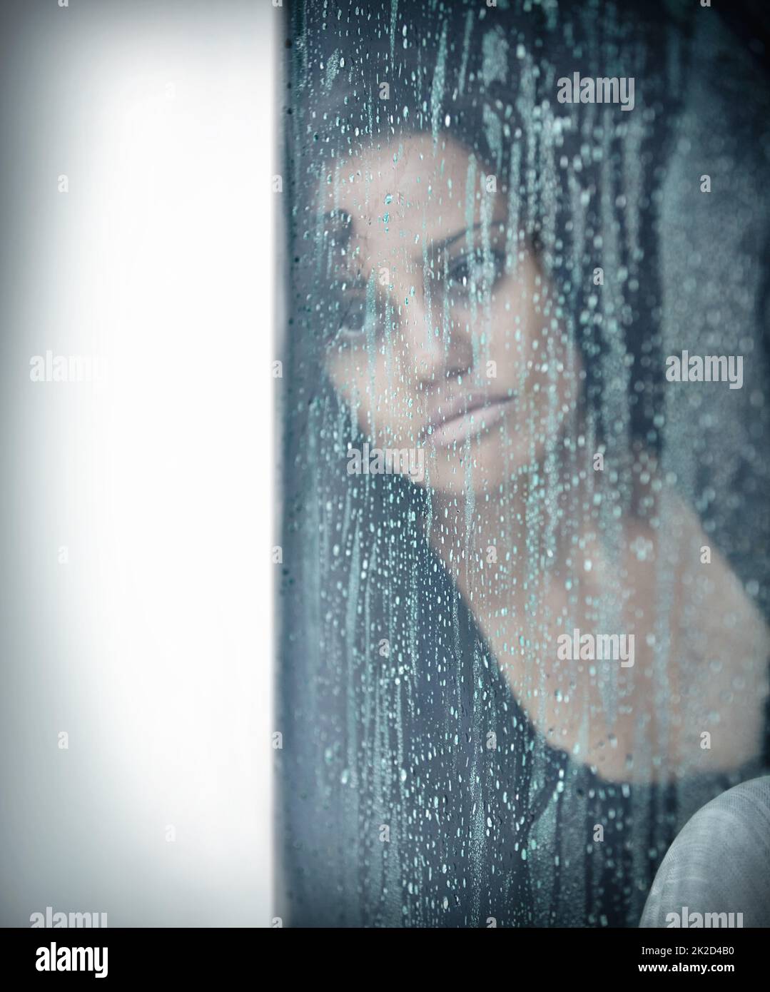 Wenn es mehr ist als nur der Blues. Eine traurige junge Frau, die an einem Fenster sitzt und draußen regnet. Stockfoto