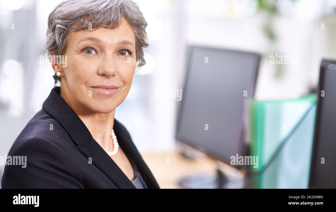 Andere im Büro schauen zu ihr auf. Porträt einer reifen Frau, die in einem Büro sitzt. Stockfoto