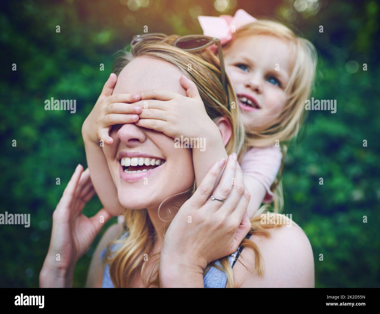 Guck mal, wer. Aufnahme eines entzückenden kleinen Mädchens, das die Augen ihrer Mutter spielerisch im Freien bedeckt. Stockfoto