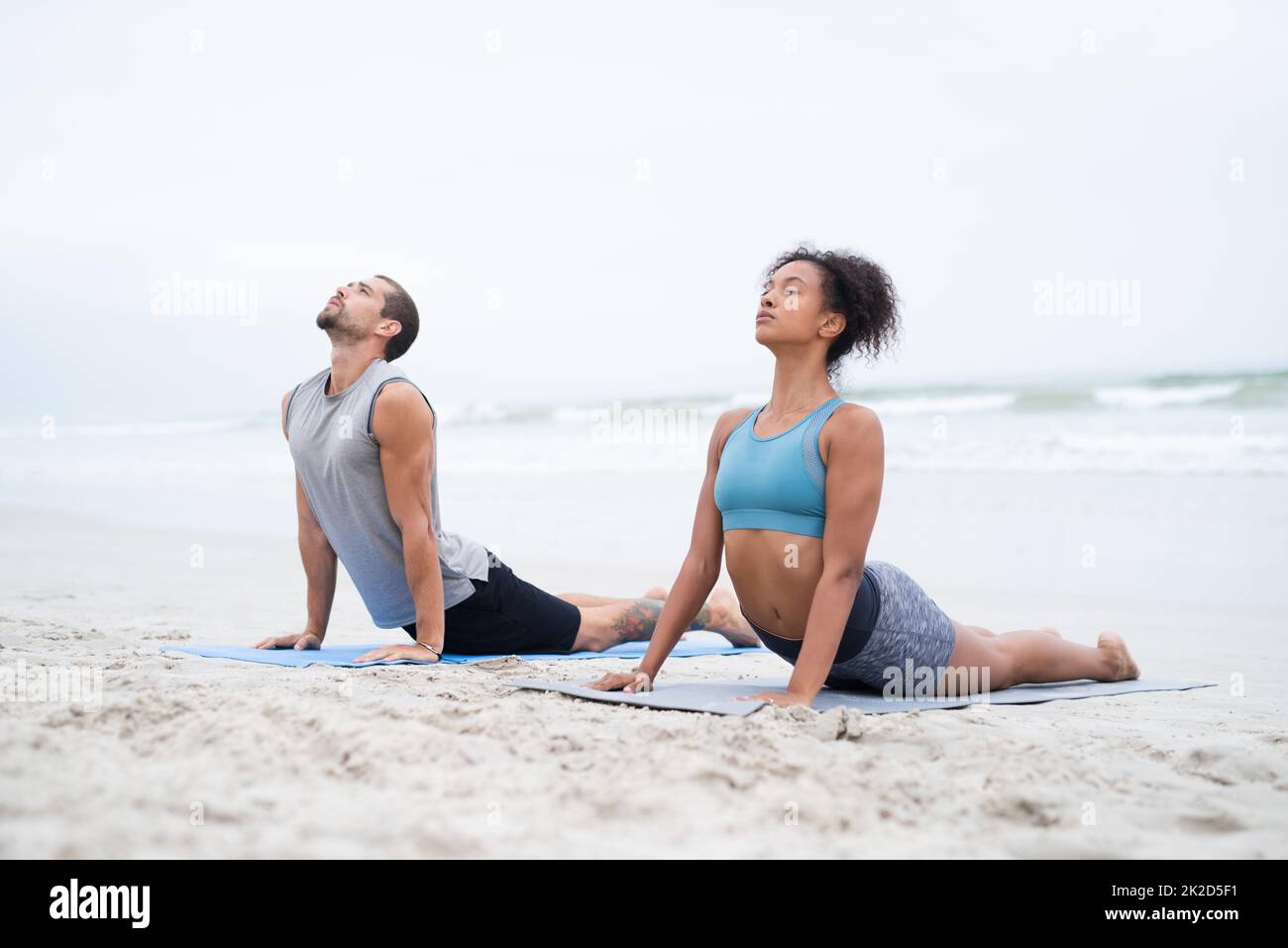 Lassen Sie alle Ihre Sinne ein Gefühl der Ruhe spüren. Aufnahme eines jungen Mannes und einer jungen Frau, die gemeinsam am Strand Yoga praktizieren. Stockfoto