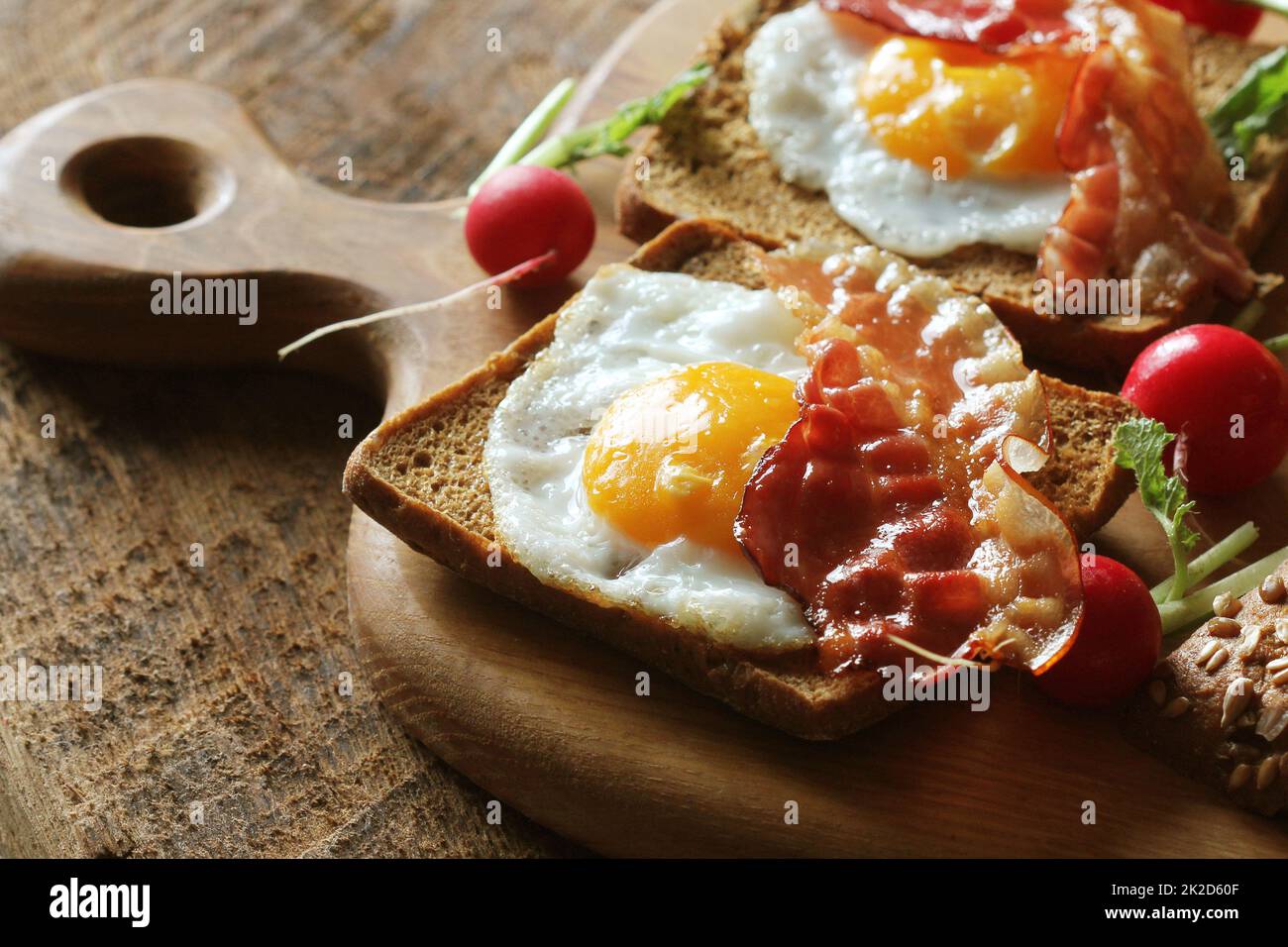 Frühstück mit knusprigem Speck, Spiegelei und Brot. Sandwiches auf Schneidebrett. Rustikale Tabelle Stockfoto