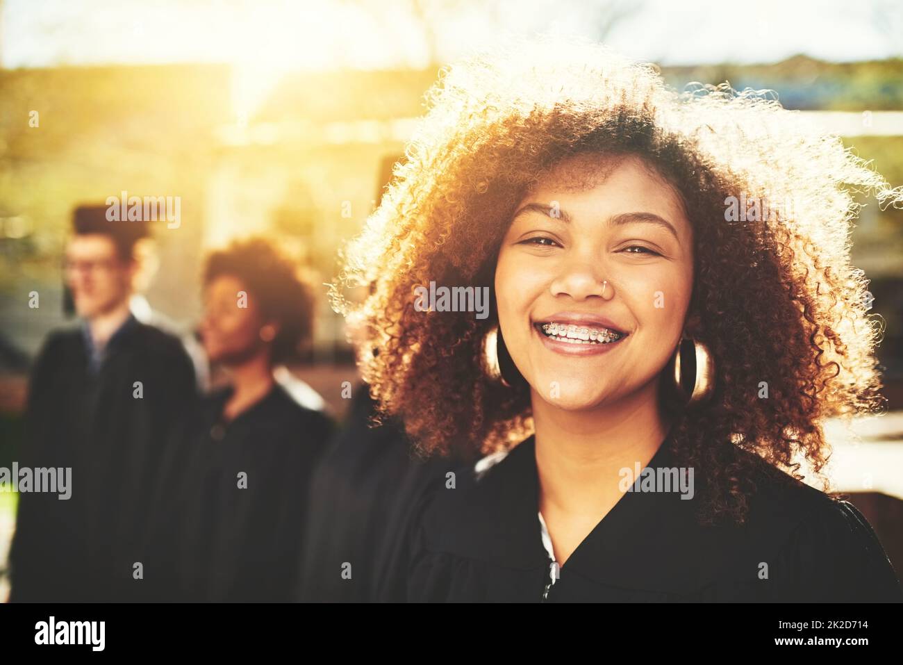 Ich bin so glücklich, meinen Abschluss zu machen. Porträt eines lächelnden Studenten am Abschlusstag mit Mitschülern im Hintergrund. Stockfoto